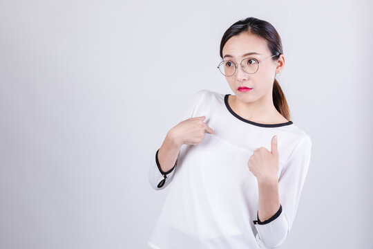 Doubtful young woman with glasses pointing at herself in studio