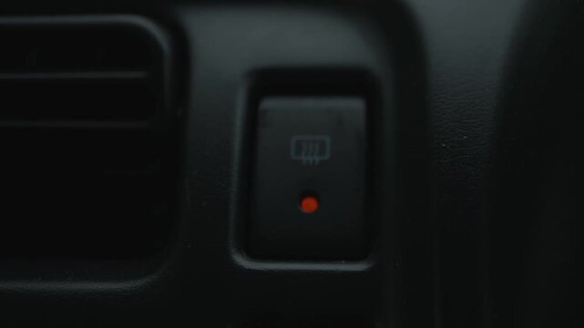  Close-up of fingers pressing rear window defroster button in car dashboard. Vehicle climate control, visibility, safety, heating, winter driving.