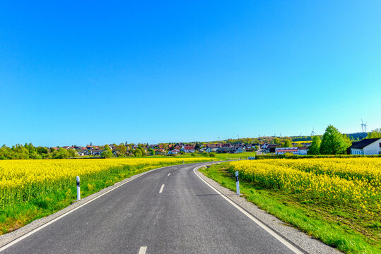 Landstra&szlig;e L3314 vorbei an bl&uuml;henden Rapsfeldern zwischen Spielberg und Wittgenborn in Hessen, Deutschland