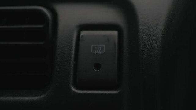 Close-up of finger pressing the rear window defroster button to turn it off, symbolizing automotive climate control, visibility, and winter driving.