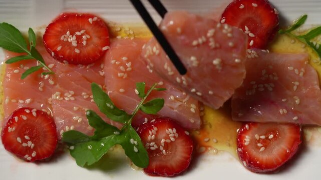 Salmon sashimi with fresh strawberry slices and sesame seeds, close up. Top view of salmon carpaccio or sashimi served with strawberry slices rucola and chopsticks