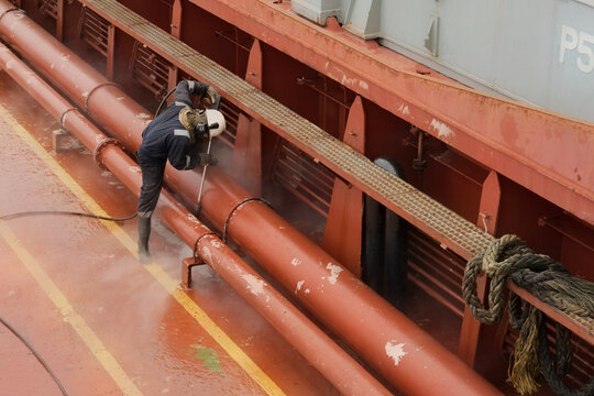 operating a high-pressure hydro blaster on cargo ship conduit lines to remove deteriorated paint and corrosion during scheduled vessel maintenance