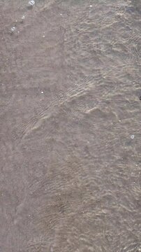 Top view of clear sea water lapping on a shallow sand shore