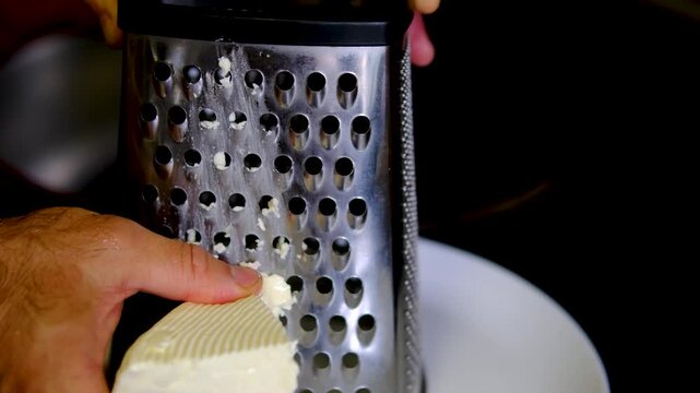 Grating bryndza cheese with hand grater for healthy homemade breakfast using fresh natural ingredients during simple everyday cooking in home kitchen