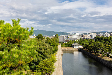 Obraz premium Historic moat of Nijo Castle Kyoto with stone walls green trees and urban skyline in background, Kyoto, Japan 