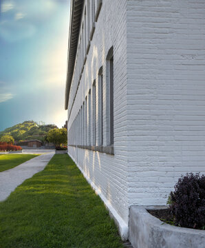A long white brick building at dusk, sidewalk, lawn and trees outside, nobody