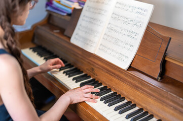 Person Playing Piano While Reading Sheet Music on an Acoustic Upright Piano © Slizo