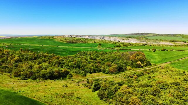 Elevated view of farmland near a quarry. Green cultivated fields and dense woodland border a distant open pit mine and rolling hills.