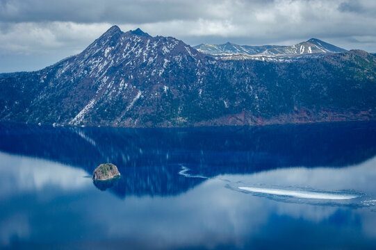 Snow-covered mountains reflecting in the mystical deep blue waters of Lake Mashu