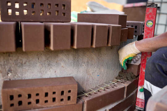 construction worker carefully applying mortar to bricks on a building site, focused and industrious mood, close-up of the bricklaying process, brown and gray bricks, concrete bricks, masoni.