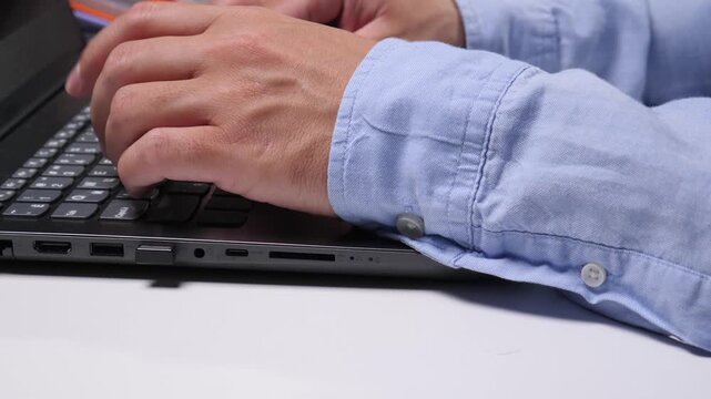 Person wearing a light blue shirt, typing on a modern laptop keyboard while working and communicating online, focusing on productivity and technology