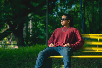 Obraz premium Young man wearing sunglasses sitting on a park bench. Man wearing sunglasses sitting in the park