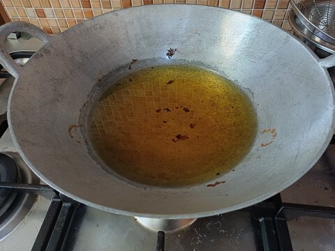 Large metal wok filled with golden cooking oil placed on gas stove. Kitchen cooking concept
