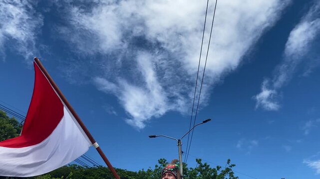 An unrecognizable person waves the Indonesian flag against a blue sky during a parade at the San Juan and San Pedro Festival in Neiva, Huila, Colombia. Concept of Indonesian culture