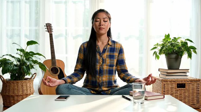 Woman practicing mindfulness seated at desk with musical instrument and houseplants nearby