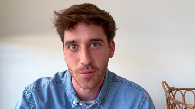 A focused young man with a beard and brown hair speaks directly to the camera, conveying a message with earnest expressions. Ideal for vlogs, tutorials, or direct communication.