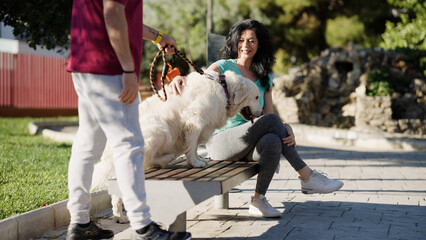 Fototapeta premium Man bringing a golden retriever dog to a woman sitting on a park bench, her petting the dog happily outdoors