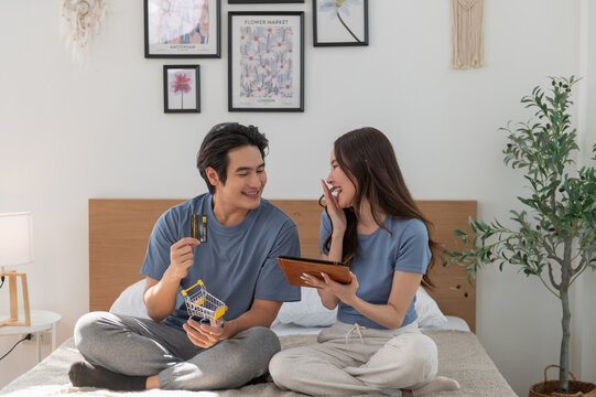 Young Asian couple shopping online while using digital tablet at home, Couple using credit card to pay bills or to book a room for vacation, making an online purchase.