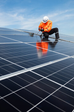 Technician installing solar panels on factory roof for green energy. A skilled technician in safety gear is working on a solar panel installation on rooftop.