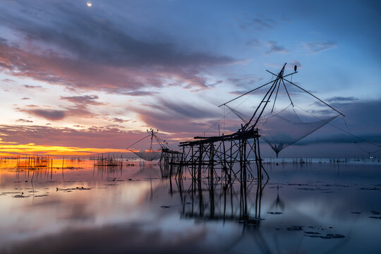 Traditional Lift Net Fishing at Pak Pra, Phatthalung During Colorful Sunrise Reflection.