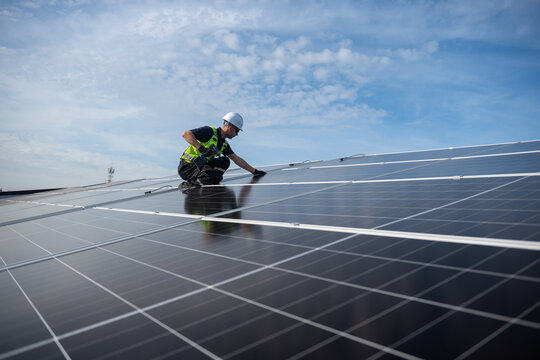 Technician installing solar panels on factory roof for green energy. A skilled technician in safety gear is working on a solar panel installation on rooftop.