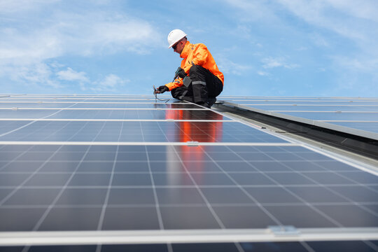 Technician installing solar panels on factory roof for green energy. A skilled technician in safety gear is working on a solar panel installation on rooftop.