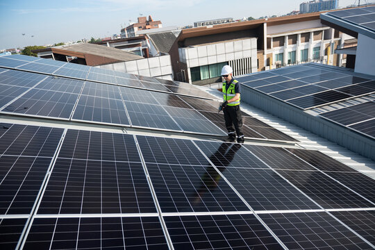 Technician installing solar panels on factory roof for green energy. A skilled technician in safety gear is working on a solar panel installation on rooftop.