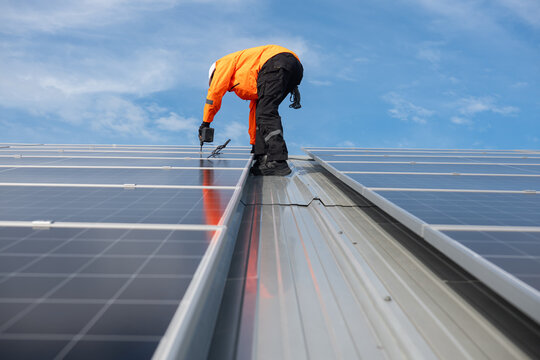 Technician installing solar panels on factory roof for green energy. A skilled technician in safety gear is working on a solar panel installation on rooftop.