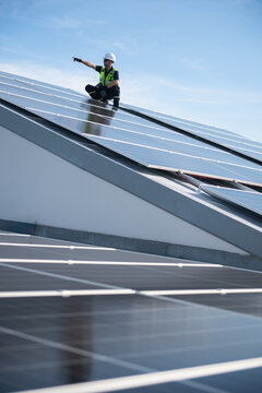Technician installing solar panels on factory roof for green energy. A skilled technician in safety gear is working on a solar panel installation on rooftop.