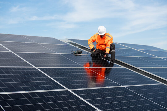 Technician installing solar panels on factory roof for green energy. A skilled technician in safety gear is working on a solar panel installation on rooftop.