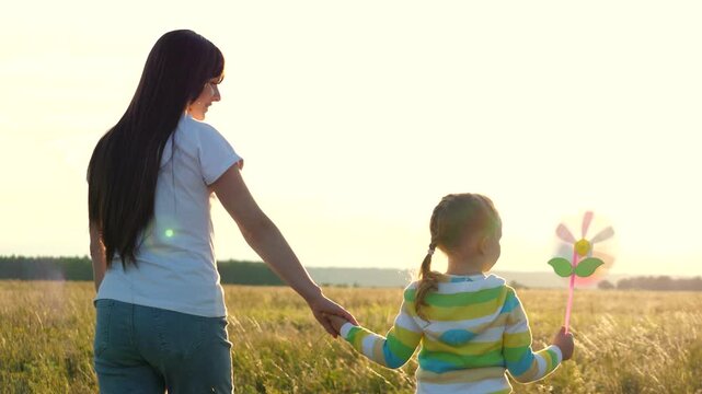 turn pinwheel windmill. mother child little girl holding hands playing parenting game together park. enjoying their time outdoors happy family creating childhood memories chasing dream. sun sets