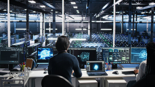 Software programmer enters a server room office and uses AI diagnostics to review infrastructure performance in a high tech facility.