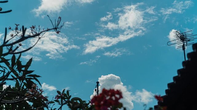Beautiful motion of white clouds with blue sky in timelapse, isolated by plumeria trees and rooftop as foreground. 4K horizontal time lapse footage. Landscape concept