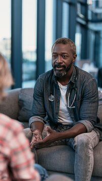 Doctor in casual attire discusses patient's health concerns while sitting on a couch