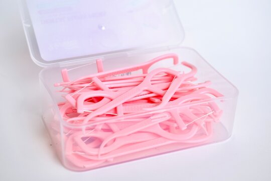 High angle close up of a plastic storage box filled with pink dental floss picks on a white background.