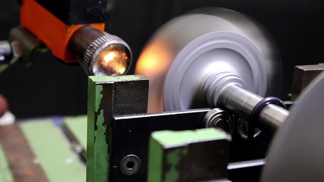 Close-up of a metallic turbocharger turbine rotor wheel mounted on a balancing machine shaft for precision calibration in an engineering workshop.