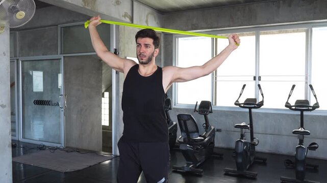 Man stretching with resistance band overhead during shoulder mobility workout in modern gym, focusing on flexibility, strength training, and functional fitness exercise.