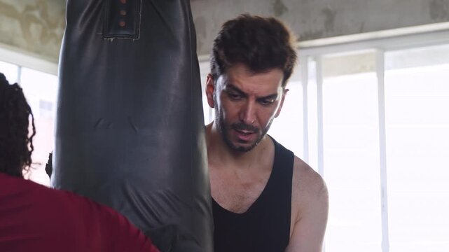 Boxing coach instructing a female student beside a punching bag in a gym, promoting boxing skills, personal training, fitness and combat sports.