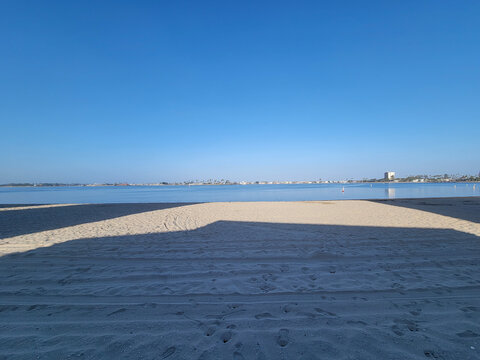 Long early morning shadows and calm still reflective water at Sail Bay beach, San Diego, California