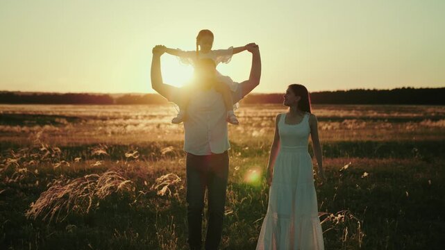 Uncle takes walk carrying niece on shoulders giving real parents break. Uncle teaches little niece to play plane and enjoys life while parents at work. Uncle plays with niece near own wife at sunset