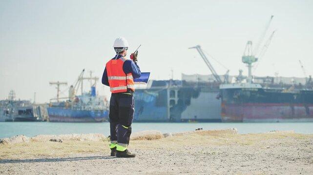 Marine engineers use a tablet to supervise cargo operations, container transport and logistics infrastructure at a commercial port, harbor, infrastructure, distribution, freight, commercial shipping.