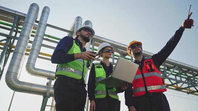 Petrochemical engineers reviewing data on a laptop at a refinery, discussing operations, industrial safety and energy infrastructure.