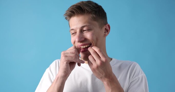 Happy young man cleaning his teeth with dental floss on light blue background