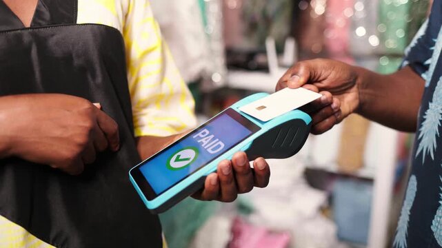 Contactless payment, African businesswoman using a pos terminal to complete a credit card transaction in her fabric retail shop
