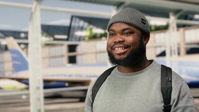 Close up of joyous man walking in airport terminal, wearing backpack, happy African American tourist moves through airport terminal, going to airplane departure gate, excited to start vacation.