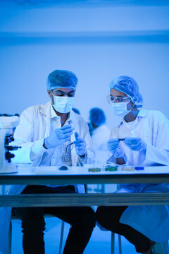 Science colleagues intently examine specimens under blue light with microscope and samples in a high-technology biolab as part of advanced scientific research with professional expertise.