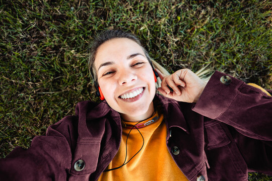 Happy woman listening music with vintage headphones at park city - Girl doing selfie lying on grass - Nostalgia lifestyle trend