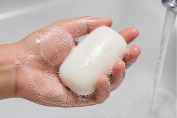 Fototapeta premium A person washes a bar of soap under running water in a sink. The soap is covered in bubbles and appears clean. This scene takes place in a kitchen or bathroom.