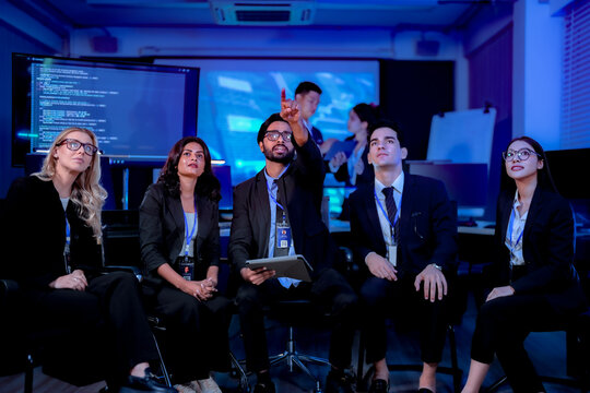 Delighted colleagues applauding and raising arms during a team win applauding the record quarter in a dark blue technology office at night captured in an authentic working moment.
