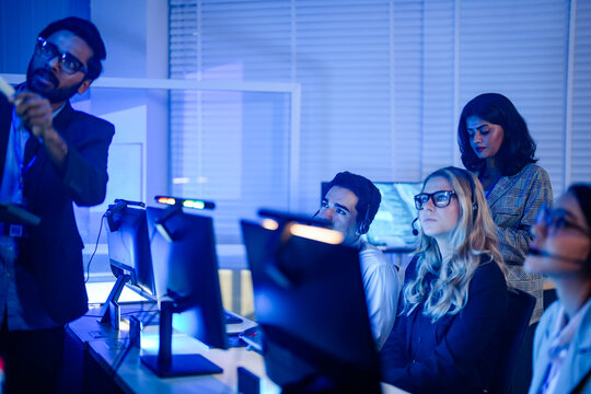Headset wearing agents raising hands during a floor training session asking about the new tool in a bright open plan support office captured in an authentic working moment.